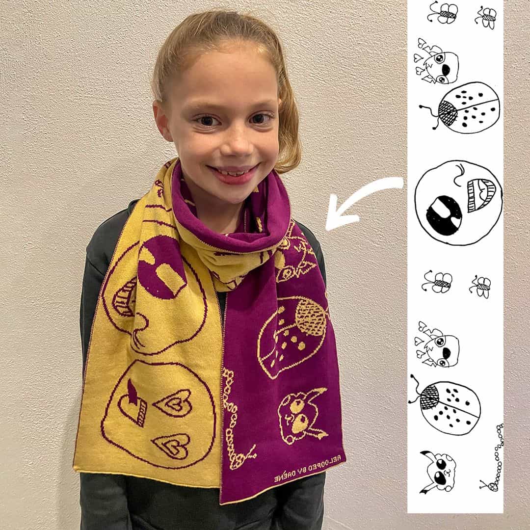 Kind draagt een gebreide kindersjaal gemaakt van een eigen tekening